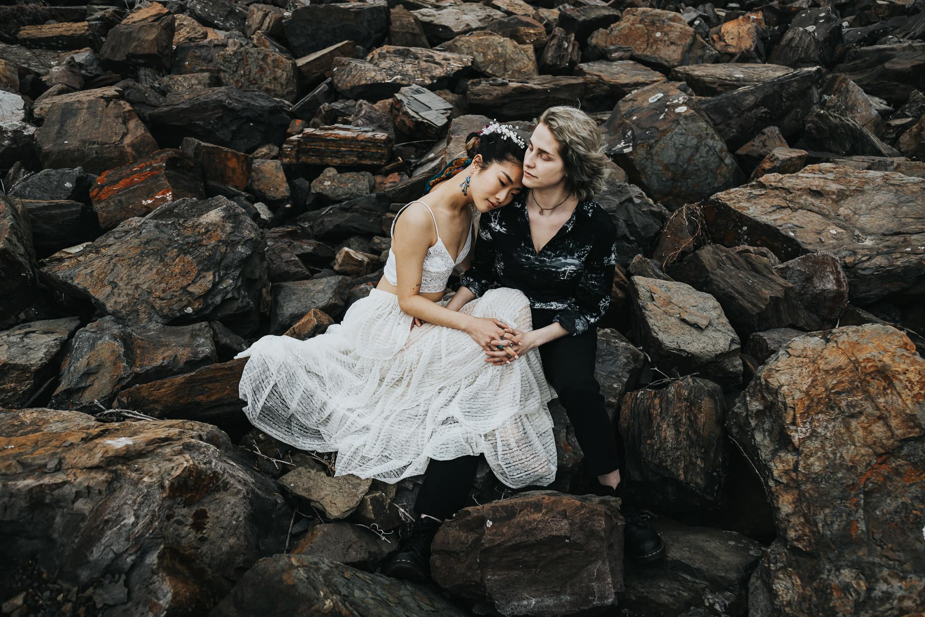 Wedding Photographer, a bride and groom sit on rocks next to the sea