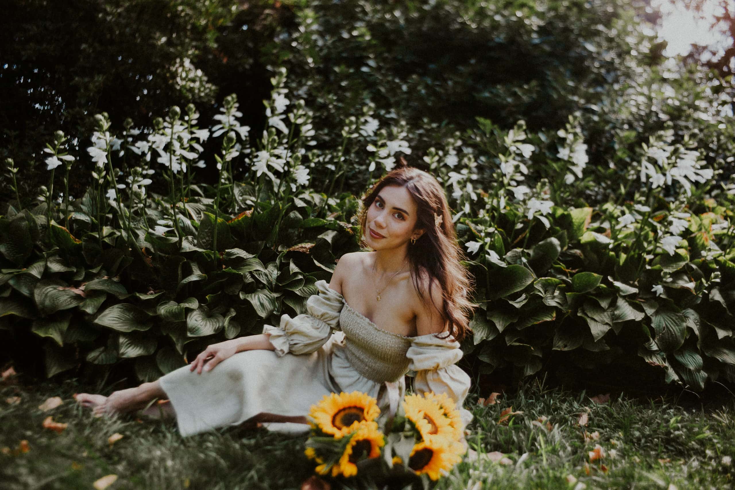 Portrait Photographer, a woman in dress sits in the grass before a lush foilage