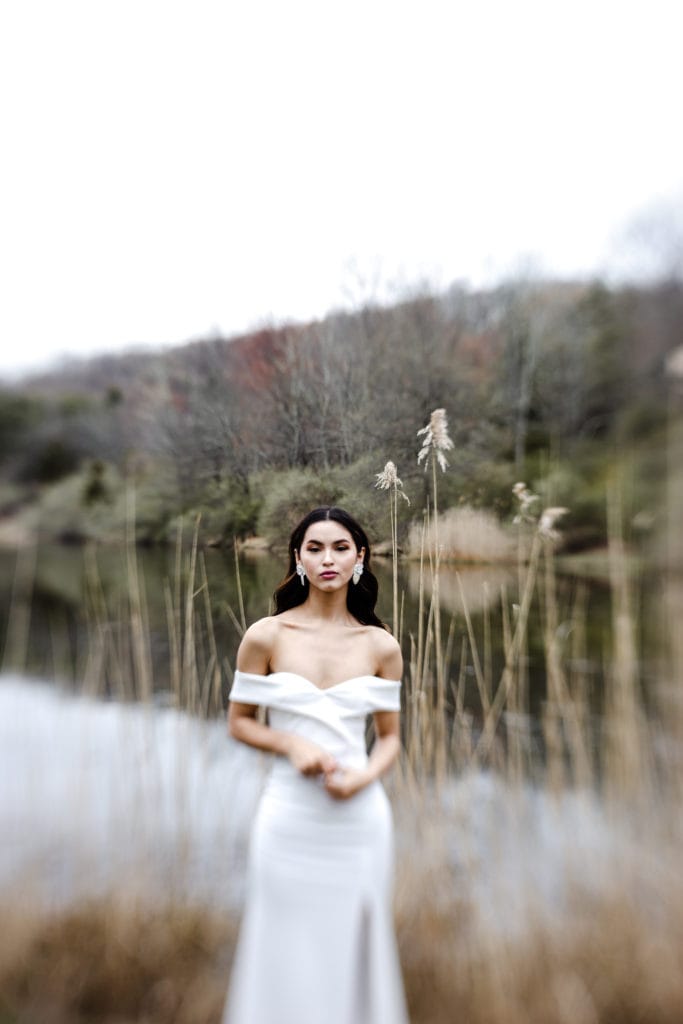 Wedding Photographer, a bride in her wedding dress stands near a quiet river and tall grass